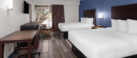 A hotel room with a desk, two beds, a chair, and a view of the outdoors.