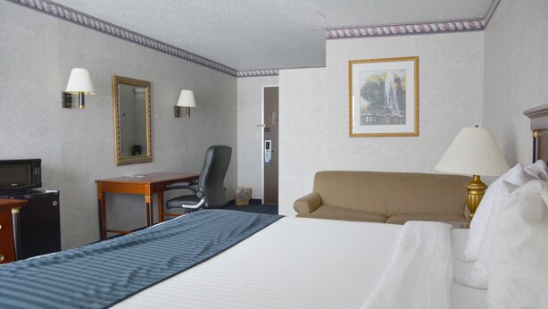 Habitación de hotel con una cama grande, un escritorio con computadora, una silla y una lámpara.