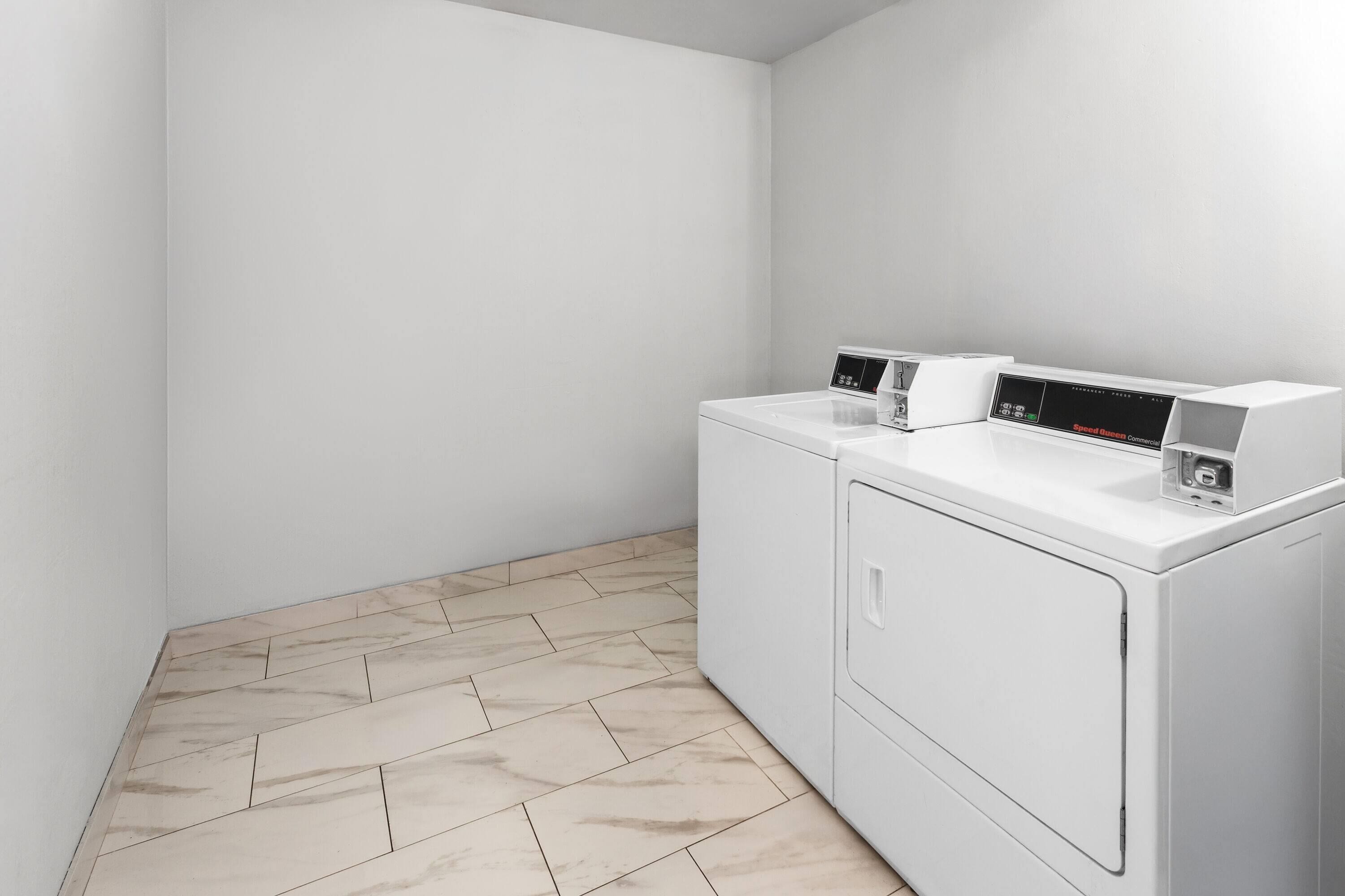 Un lavadero con lavadora y secadora de carga frontal, un panel de control y una pared blanca.