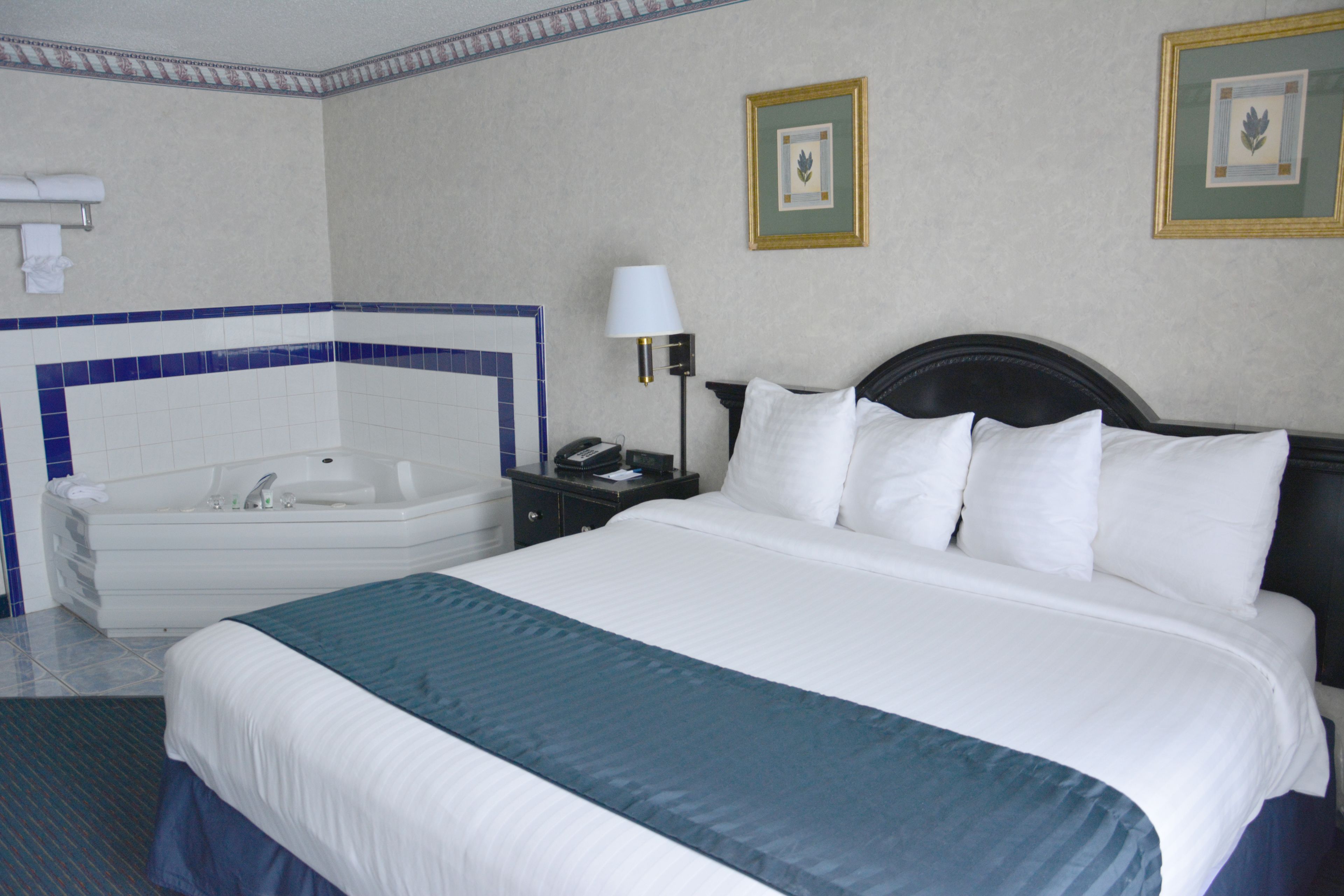 Une chambre d’hôtel avec un grand lit, une salle de bain séparée avec une baignoire, une table de chevet avec une lampe et deux tableaux encadrés au mur.