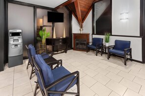 A modern living room with a fireplace, a flat-screen TV mounted on the wall, and a seating area with blue chairs. - Travelodge by Wyndham Milwaukee (Milwaukee)