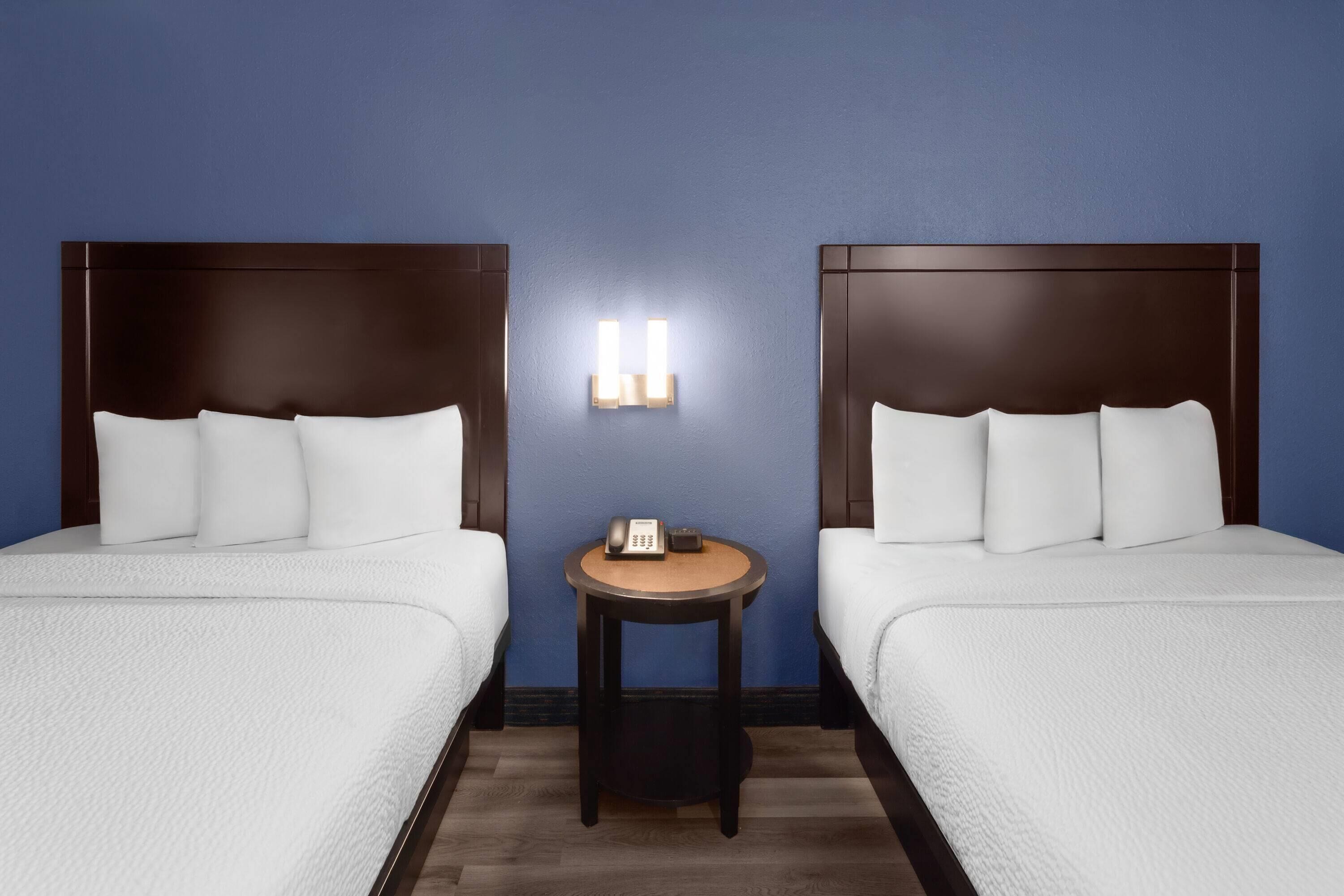 A hotel room with two beds, a small table with a telephone, and a wall-mounted light fixture.