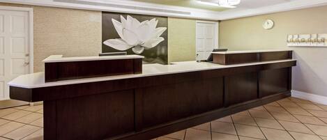 A reception desk with a dark wood finish, a white countertop, and a large white lotus flower mural on the wall.