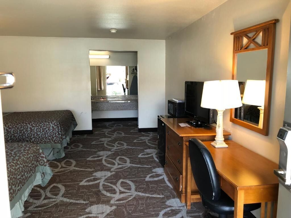 Habitación de hotel con cama, escritorio con lámpara, televisión y espejo.