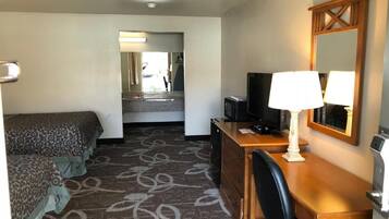 Habitación de hotel con cama, escritorio con lámpara, televisión y espejo.