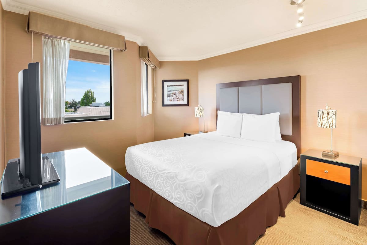 A hotel room with a large bed, a bedside table with a lamp, a window with curtains, and a framed picture on the wall.