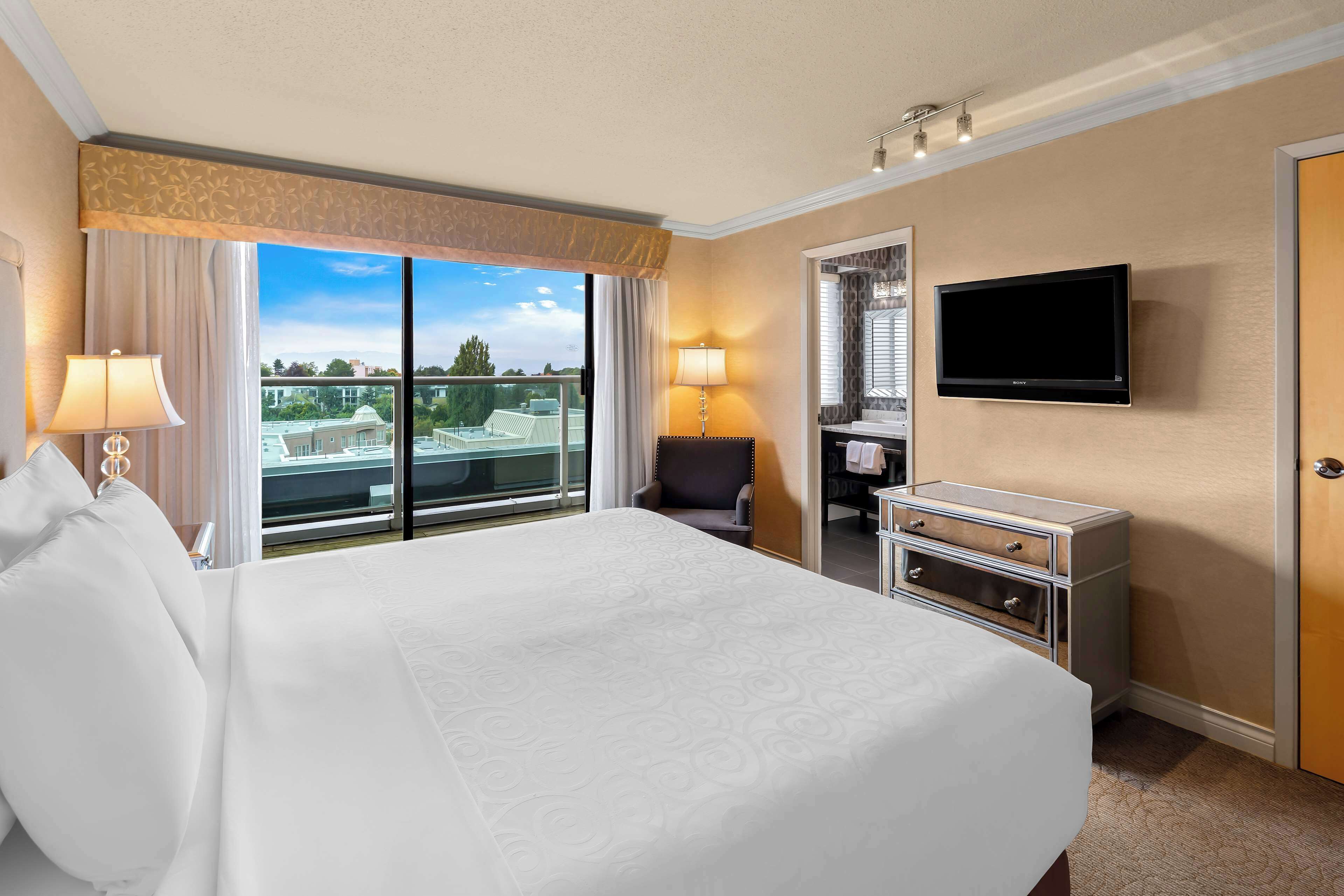 A hotel room with a large bed, a television, a desk, and a view of a cityscape.