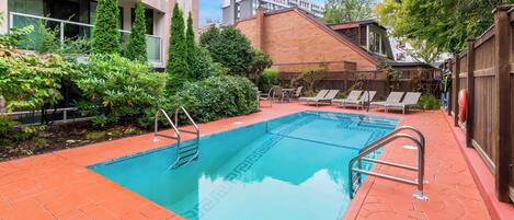 Una piscina rectangular con una escalera metálica en un lado, rodeada de suelo de baldosas rojas.