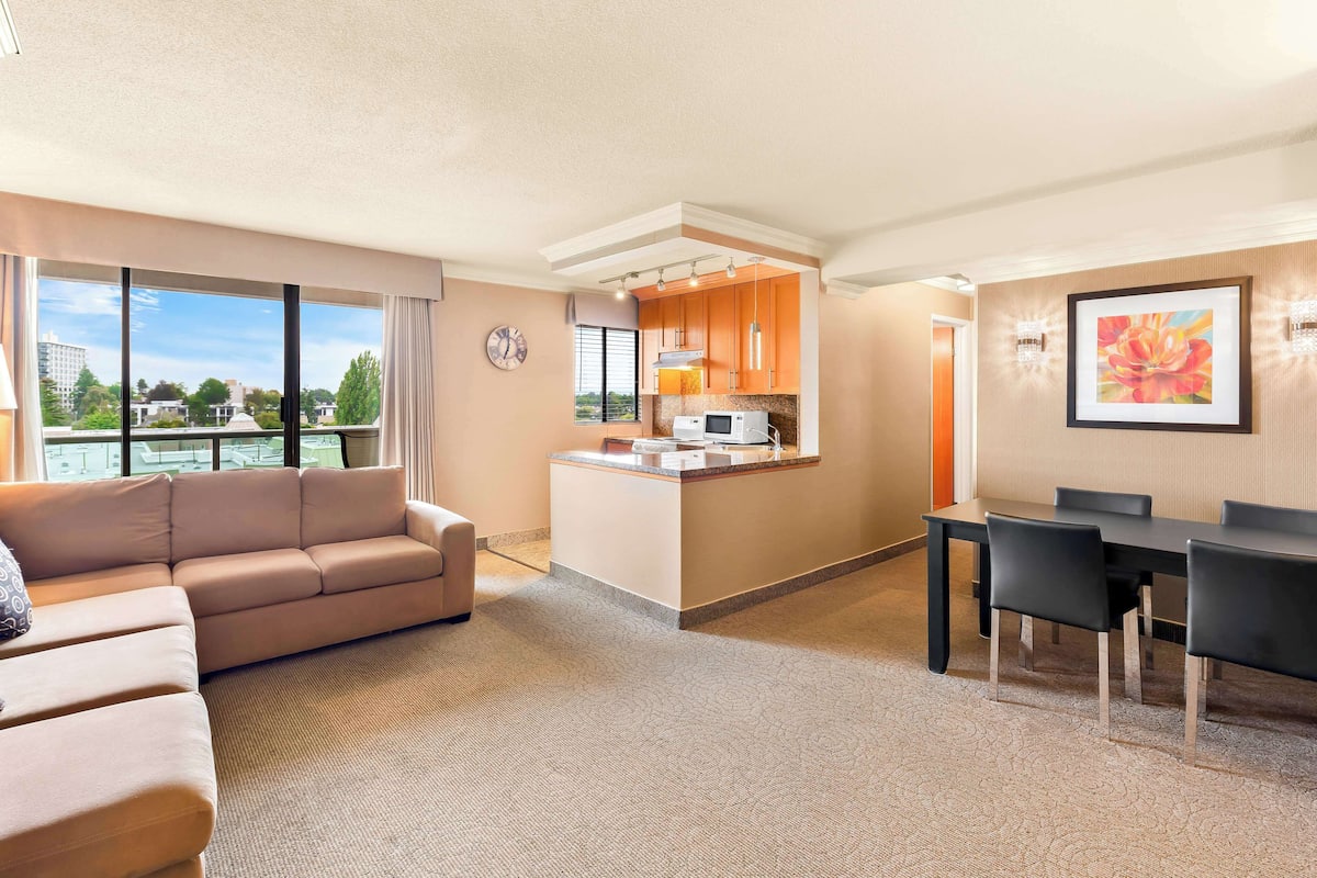 A modern hotel room with a sofa, dining table, and kitchenette.