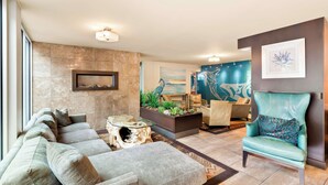 A modern living room with a sectional sofa, a glass coffee table, a teal armchair, and a fireplace. - Best Western Plus Inner Harbour (Victoria)