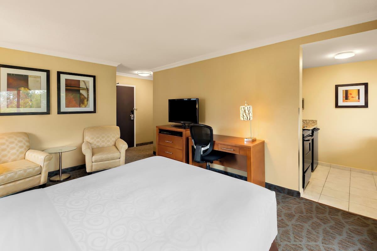 A hotel room with a bed, two armchairs, a desk with a computer, a television, and framed artwork on the walls.