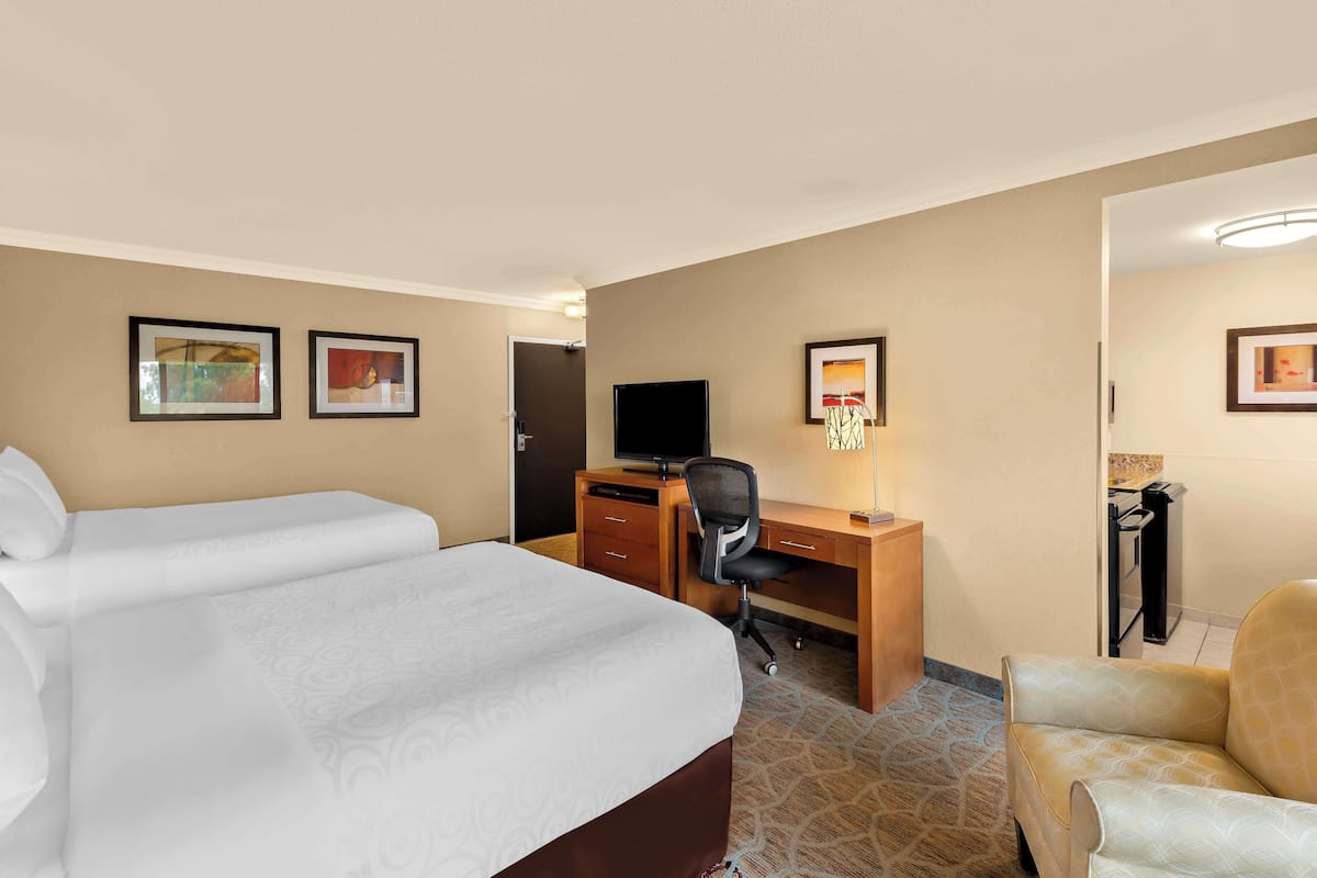 A hotel room with a large bed, a desk with a computer, a chair, and framed pictures on the walls.
