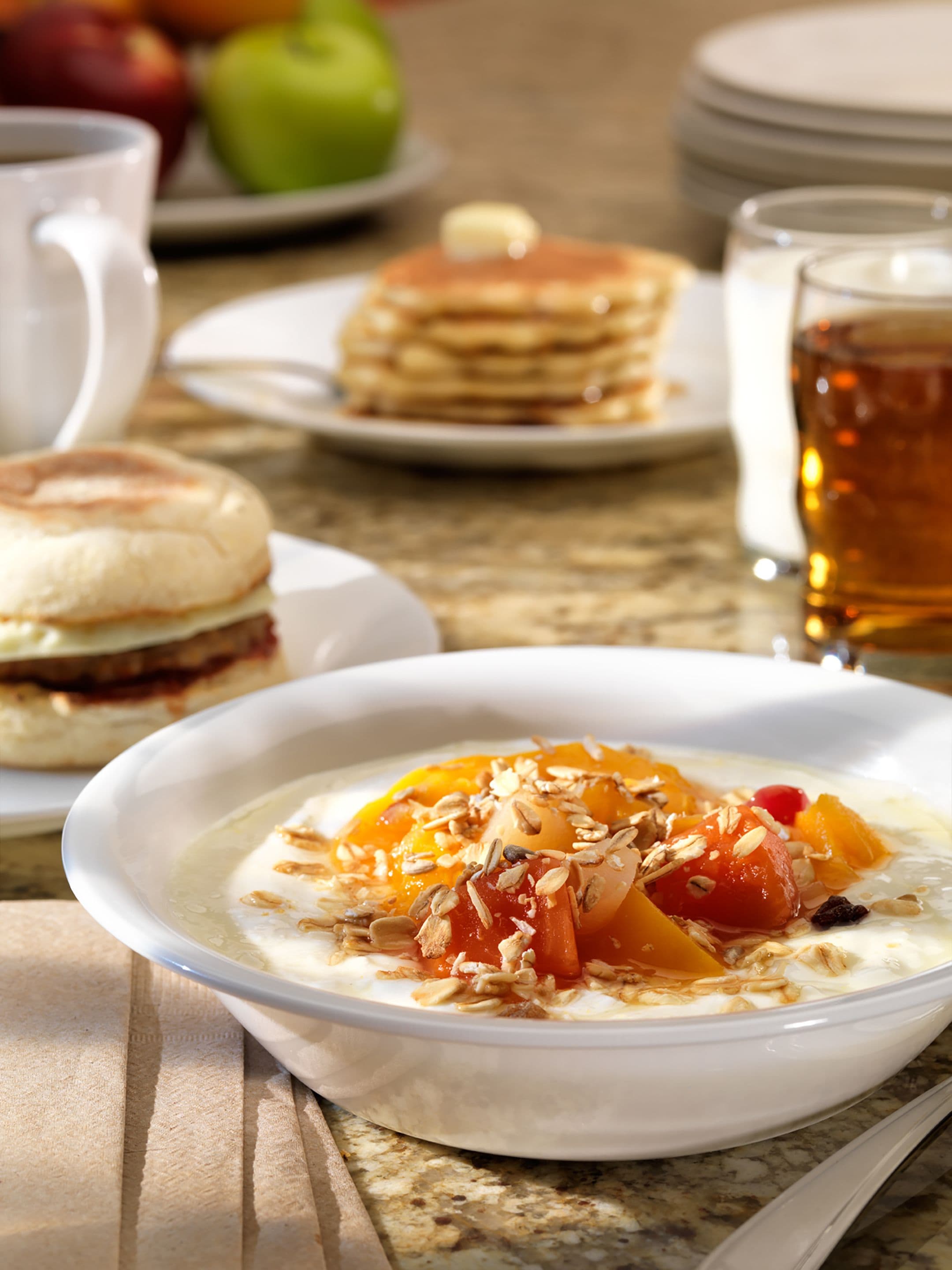 Une table mise pour le petit-déjeuner avec un bol de porridge garni de fruits et de noix, des crêpes sur une assiette et une tasse de thé.