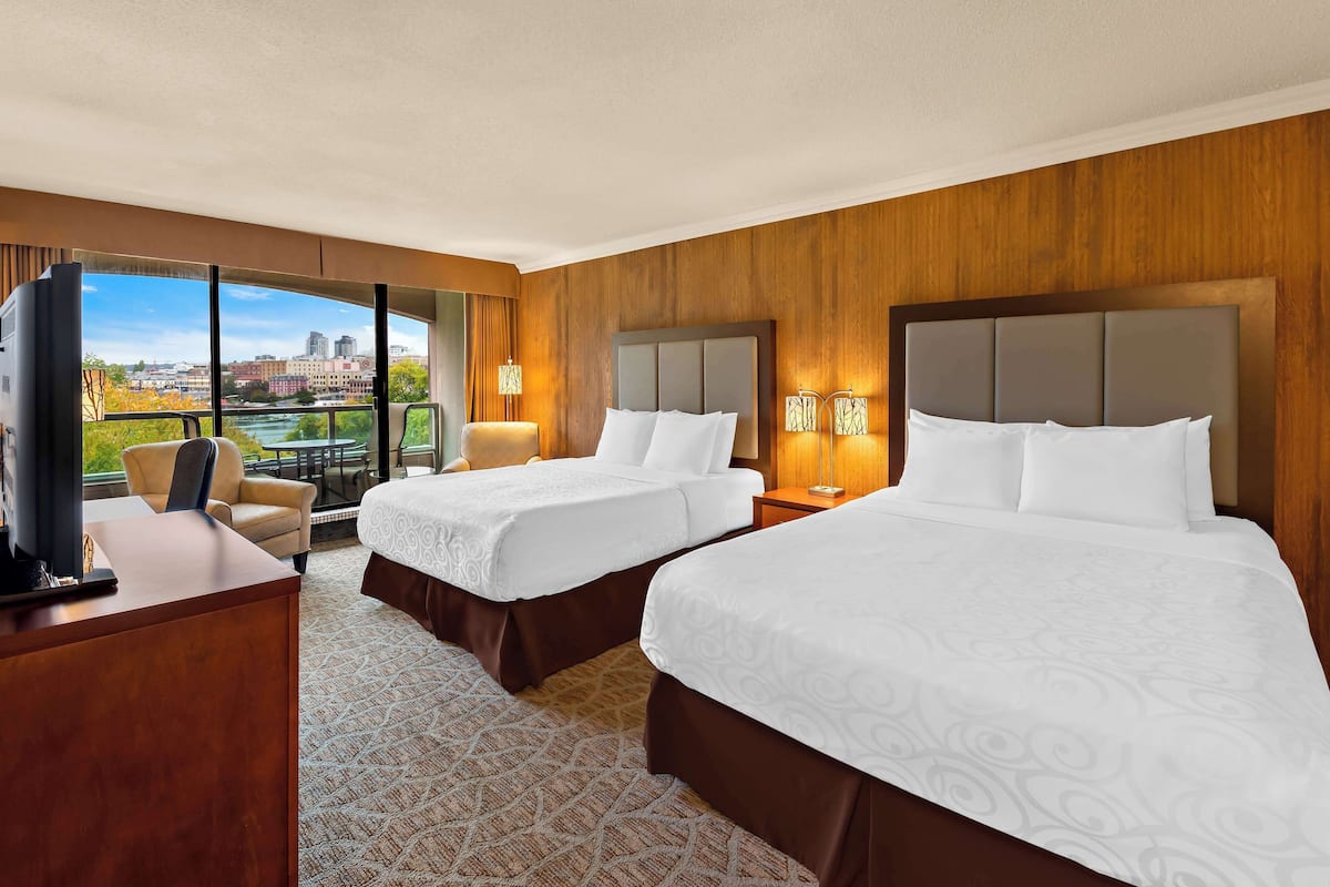 A hotel room with two beds, a desk, a TV, and a view of the city.