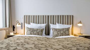 A hotel room with a striped headboard, two bedside lamps, a patterned bedspread, and a window with curtains.