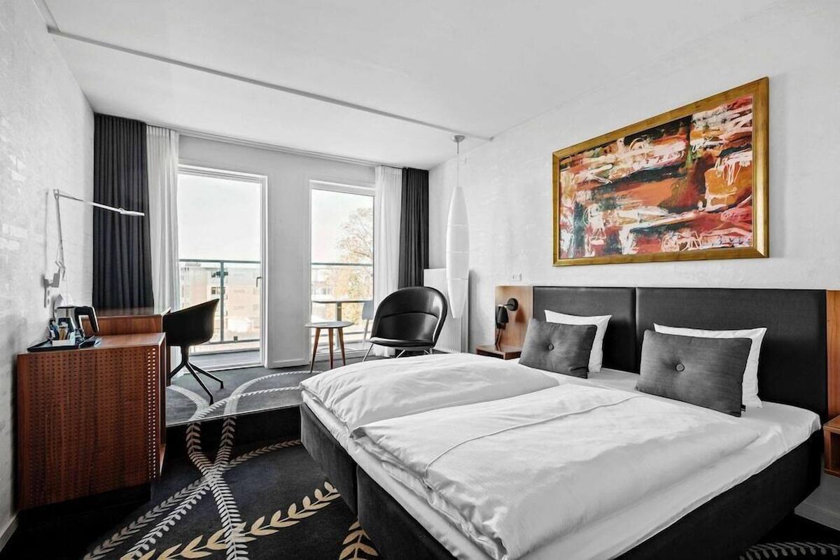 Habitación de hotel con una cama grande, un escritorio, una silla, un cuadro y vistas al exterior.