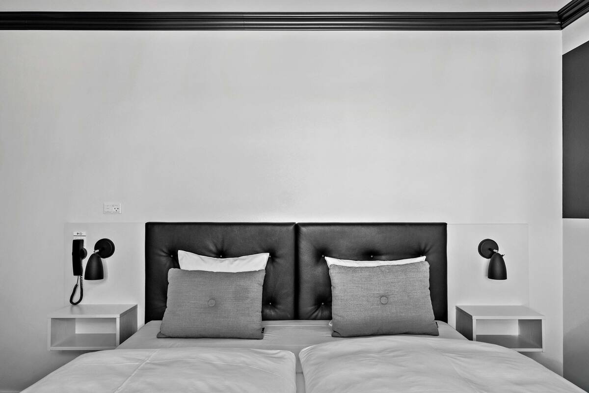 Un dormitorio moderno con una cama grande, dos mesitas de noche, un teléfono en la pared y una lámpara de pared.