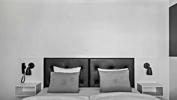 A modern bedroom with a large bed, two nightstands, a wall-mounted telephone, and a wall-mounted lamp.