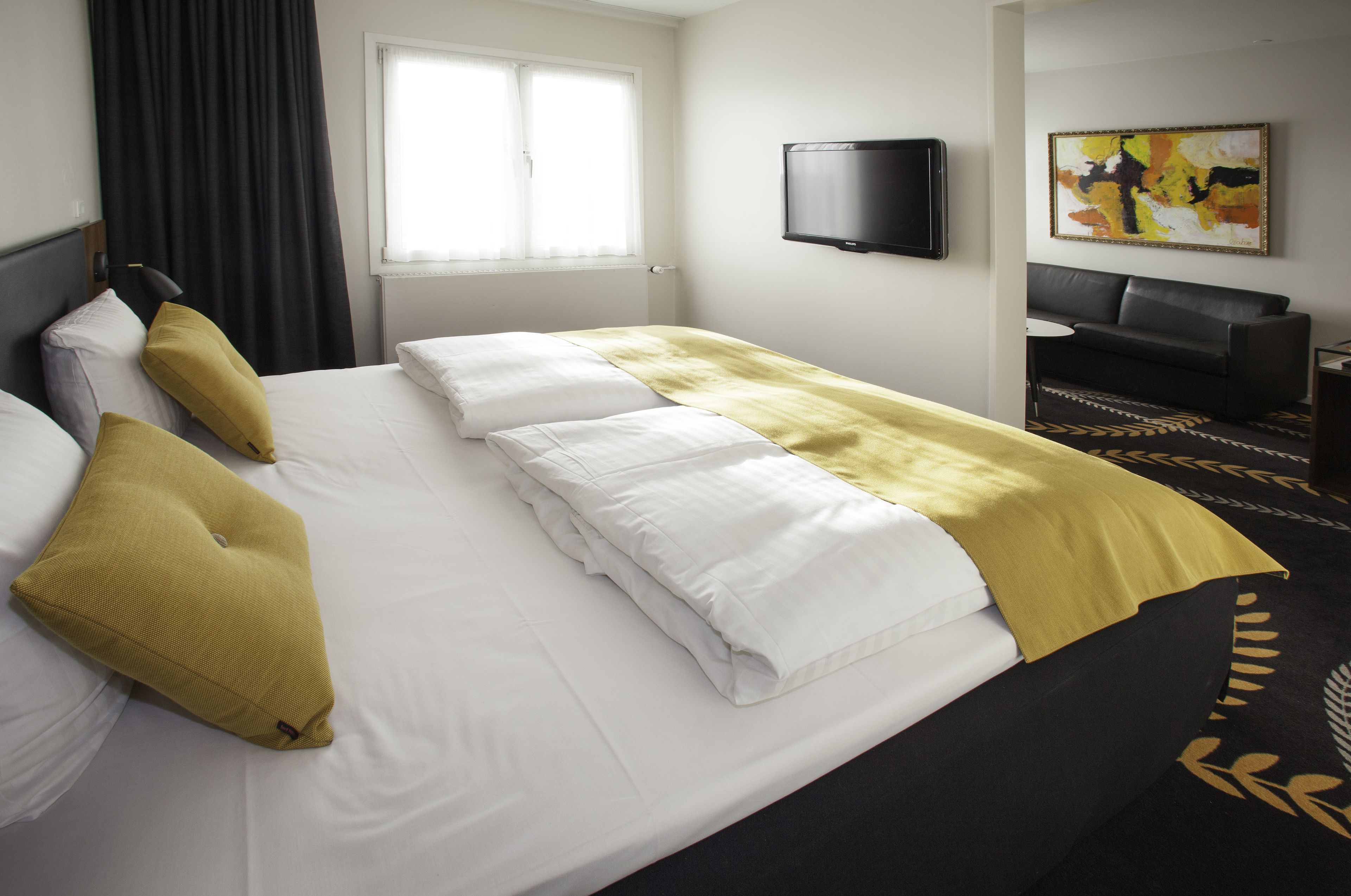 A hotel room with a bed, a television, a sofa, and a painting on the wall.