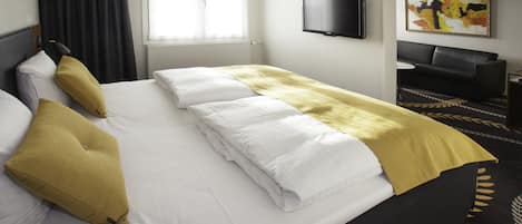 A hotel room with a bed, a television, a sofa, and a painting on the wall.