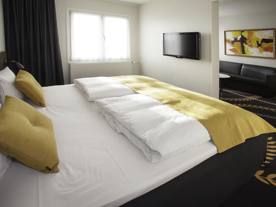 A hotel room with a bed, a television, a sofa, and a painting on the wall.