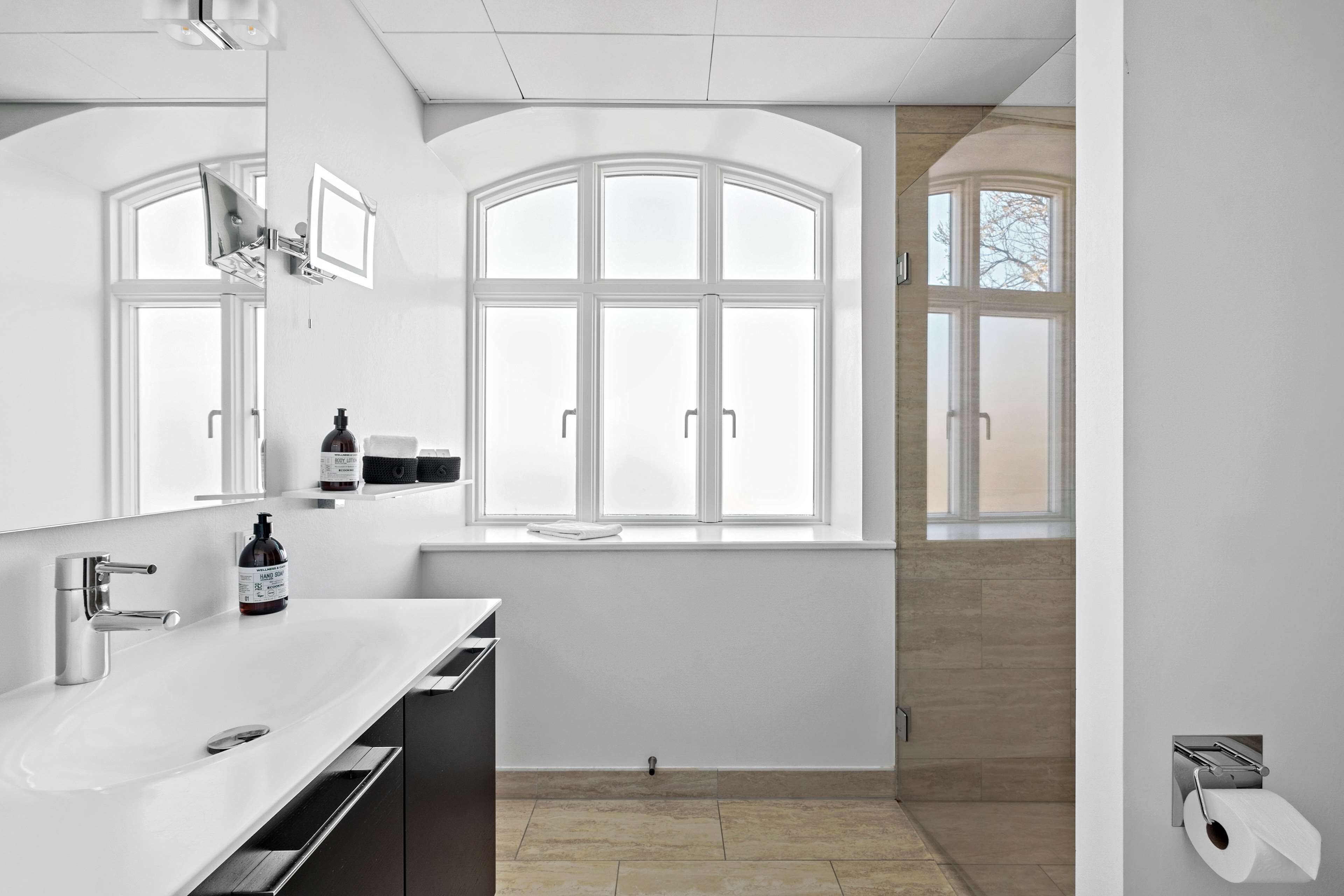 A modern bathroom with a large window, a sink, and a toilet paper holder.
