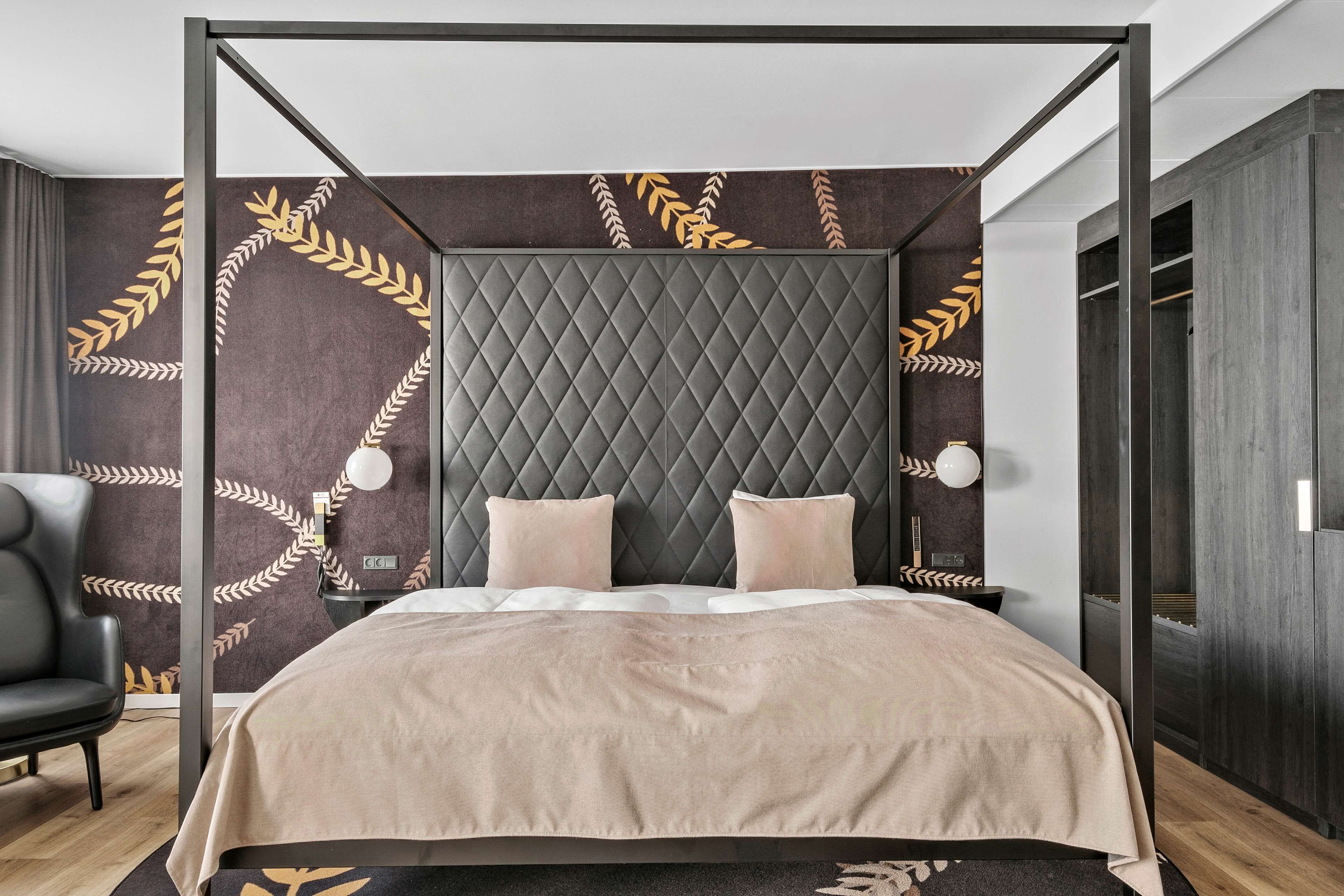 Un dormitorio moderno con un cabecero capitonado, una colcha en tonos neutros y un diseño decorativo con hojas en las paredes.