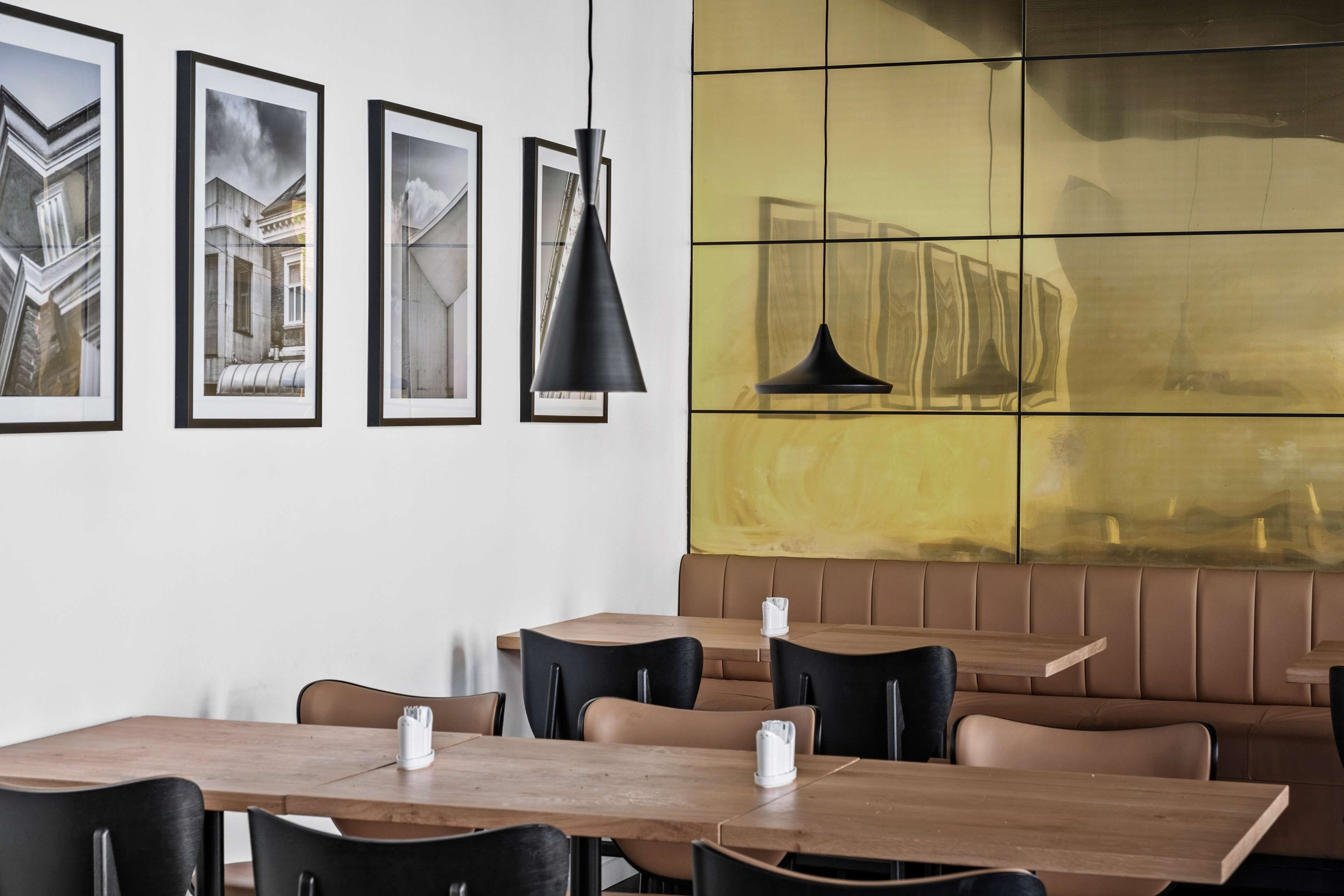 Een restaurantinterieur met houten tafels en zwarte stoelen, een geel betegelde muur en ingelijste foto's aan de muur.