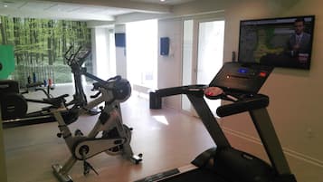 A gym with exercise equipment, a treadmill, and a large window with a forest view.