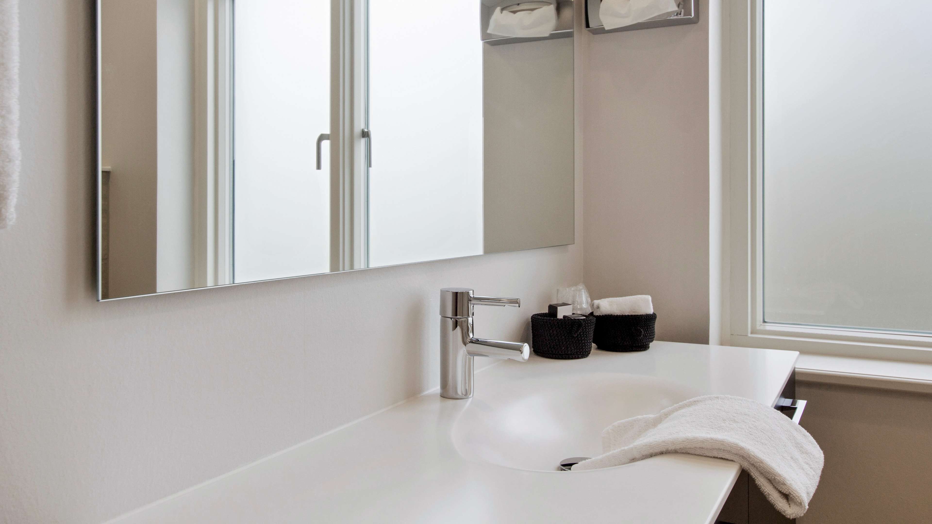 A modern bathroom with a white sink, a large mirror, and a window.
