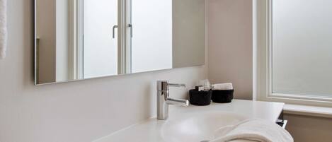 A modern bathroom with a white sink, a large mirror, and a window.