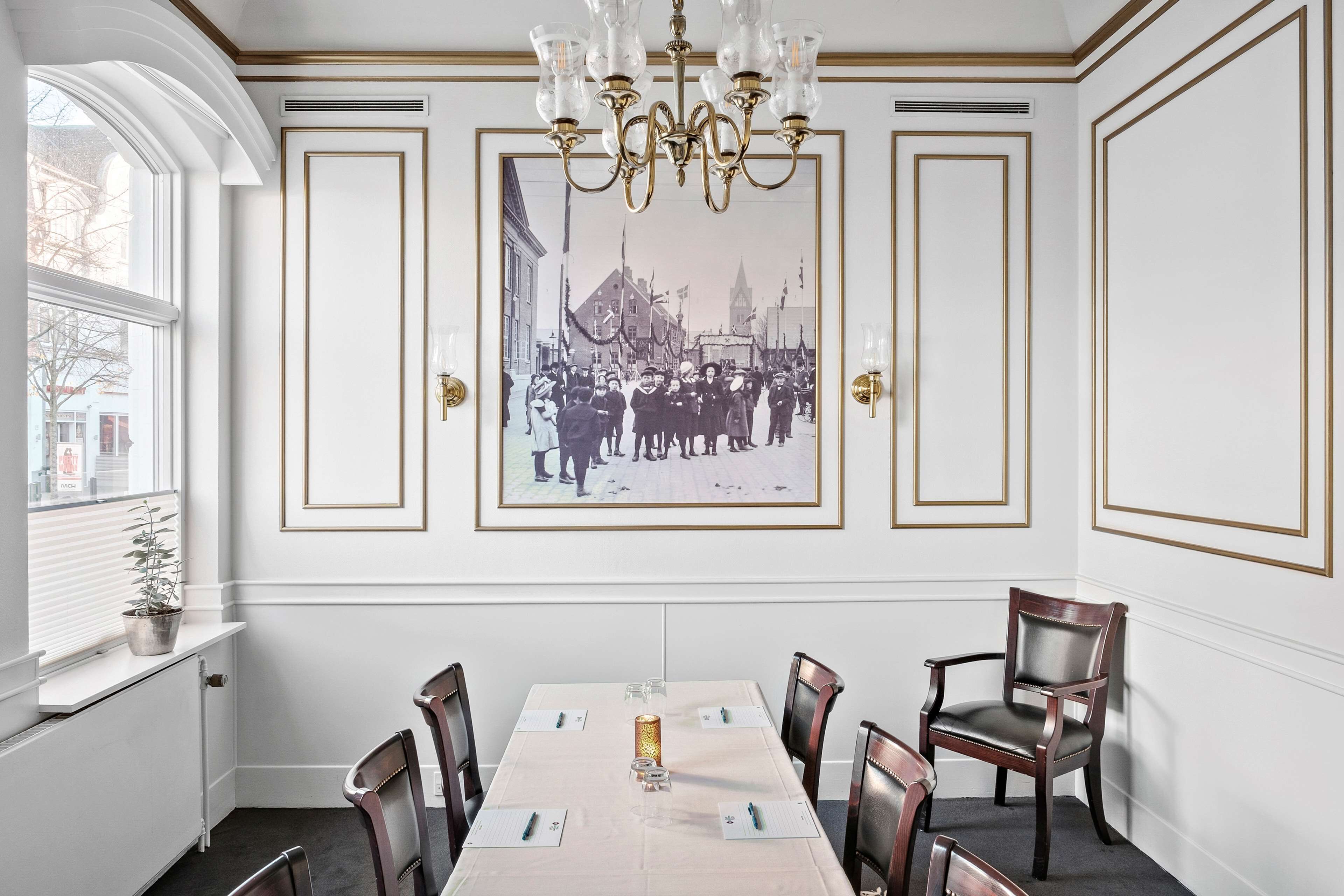 Un comedor con una larga mesa, sillas, un candelabro y una fotografía histórica enmarcada en la pared.