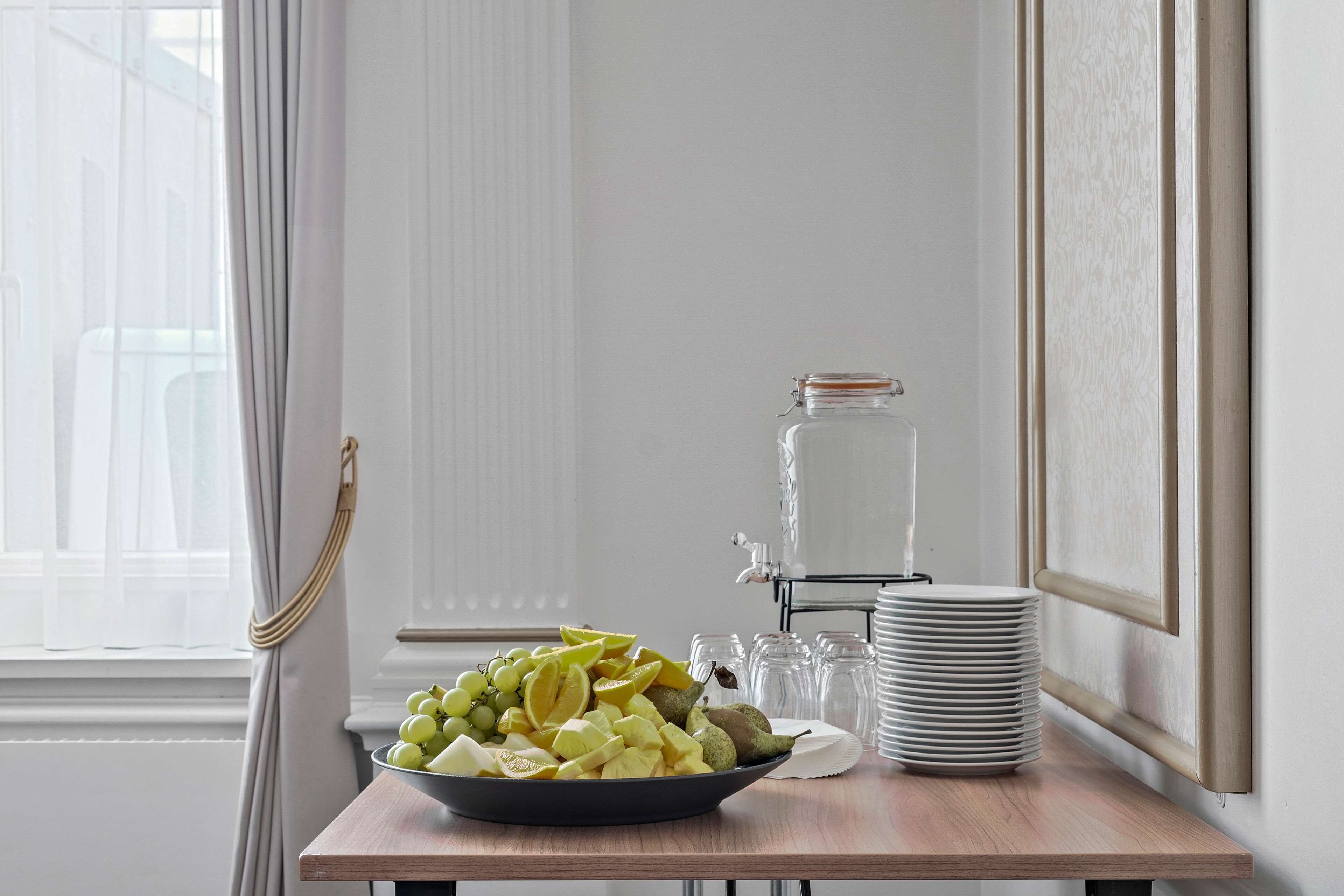 Una mesa de desayuno con un bol de fruta, una pila de platos y un dispensador de agua.