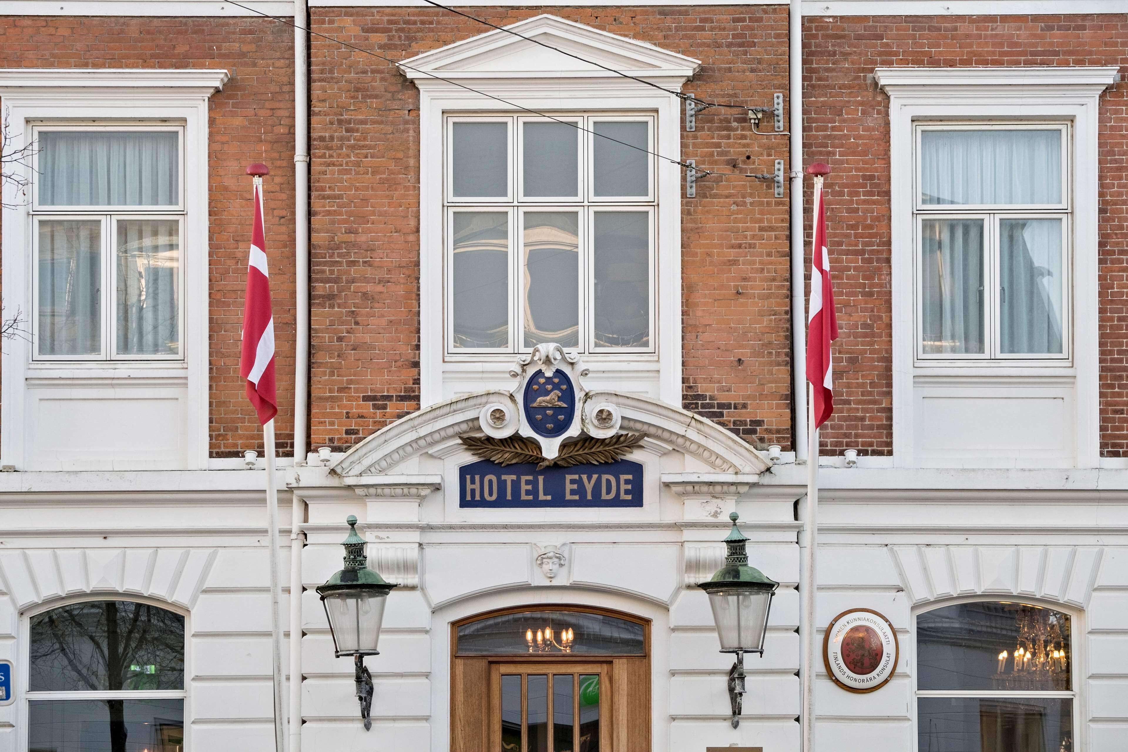 A building with a sign reading "HOTEL EYDE" above the entrance, flanked by two flags.