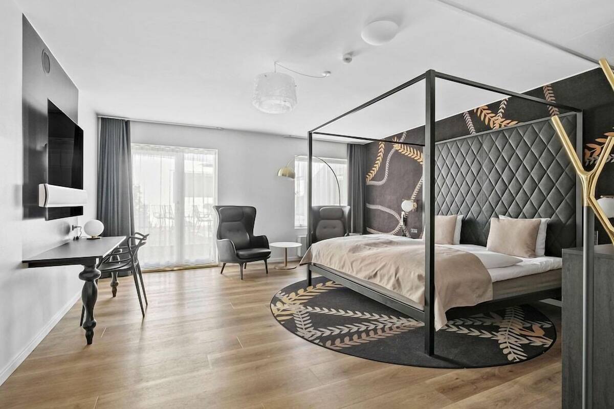 Un dormitorio moderno con una cama con dosel, un escritorio con una silla y un ventanal grande.