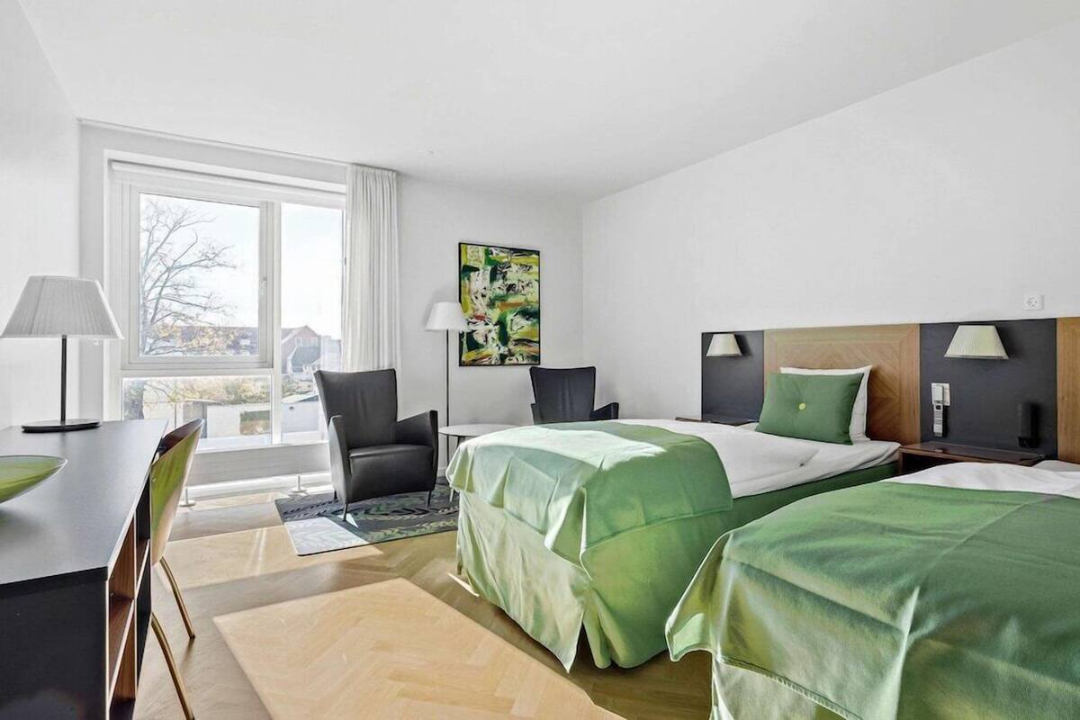 Habitación de hotel con dos camas, un escritorio, una silla, una lámpara y un cuadro en la pared.