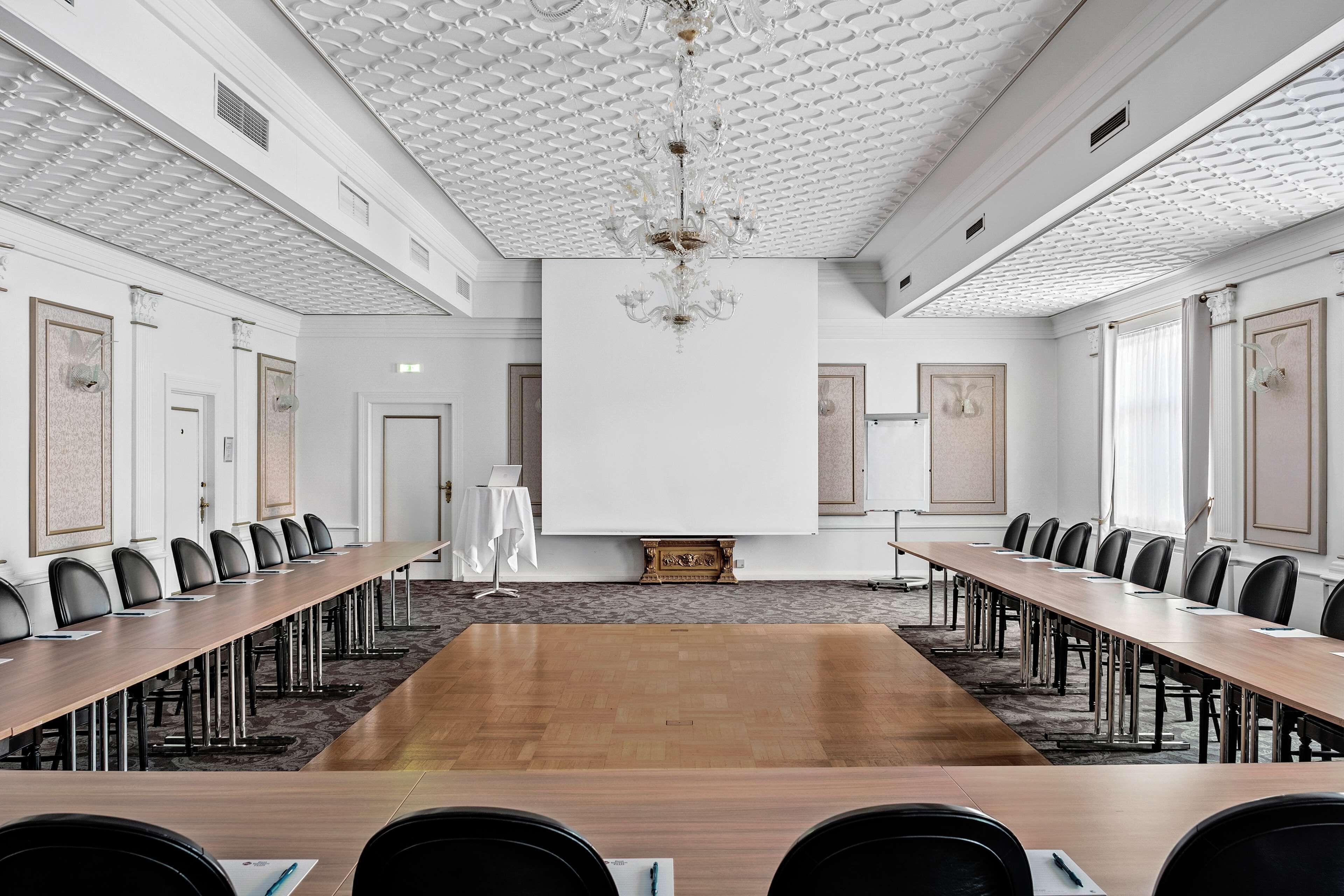 Una sala conferenze con un lungo tavolo, diverse sedie e un lampadario.