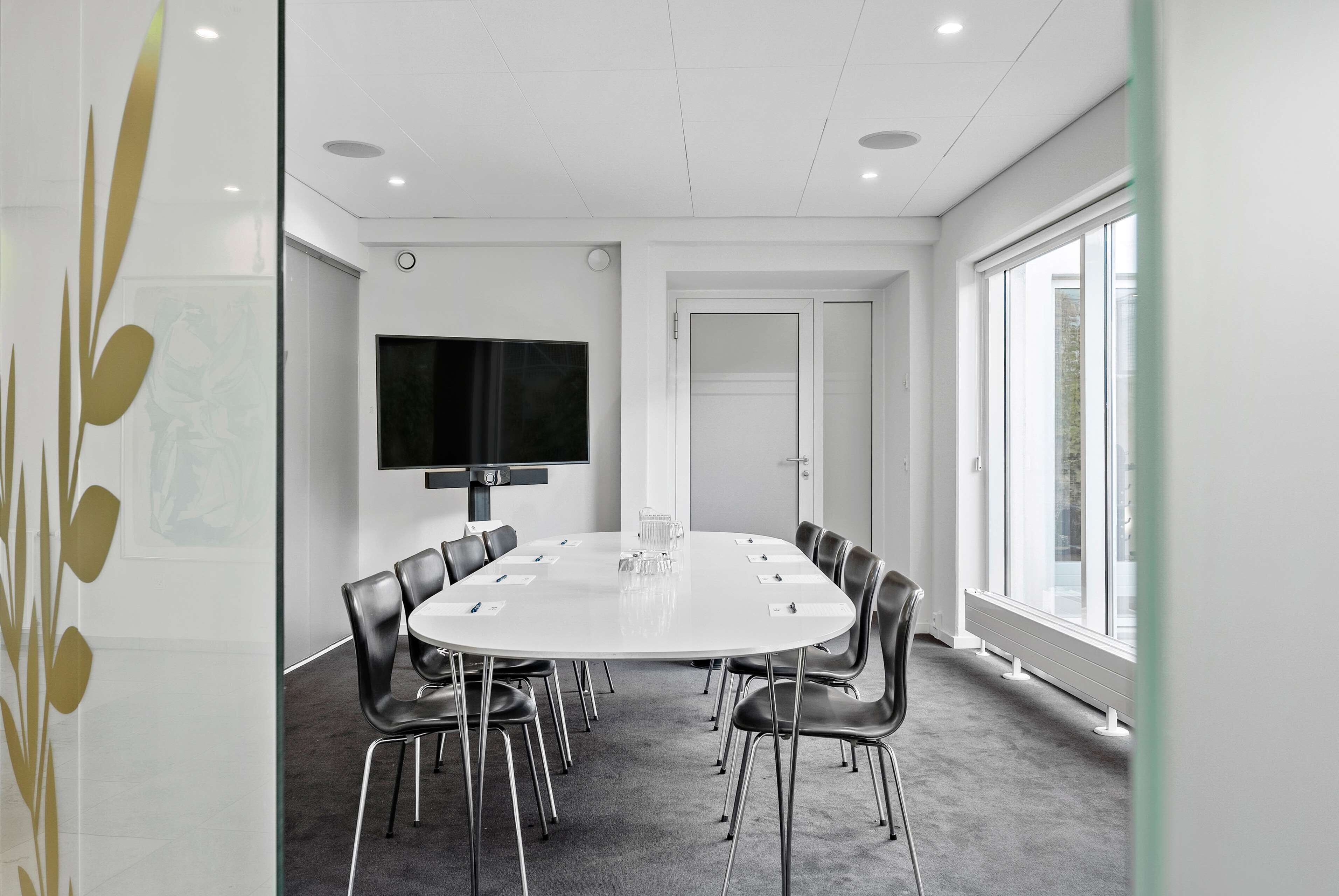 A conference room with a white table, black chairs, a TV, and a door.