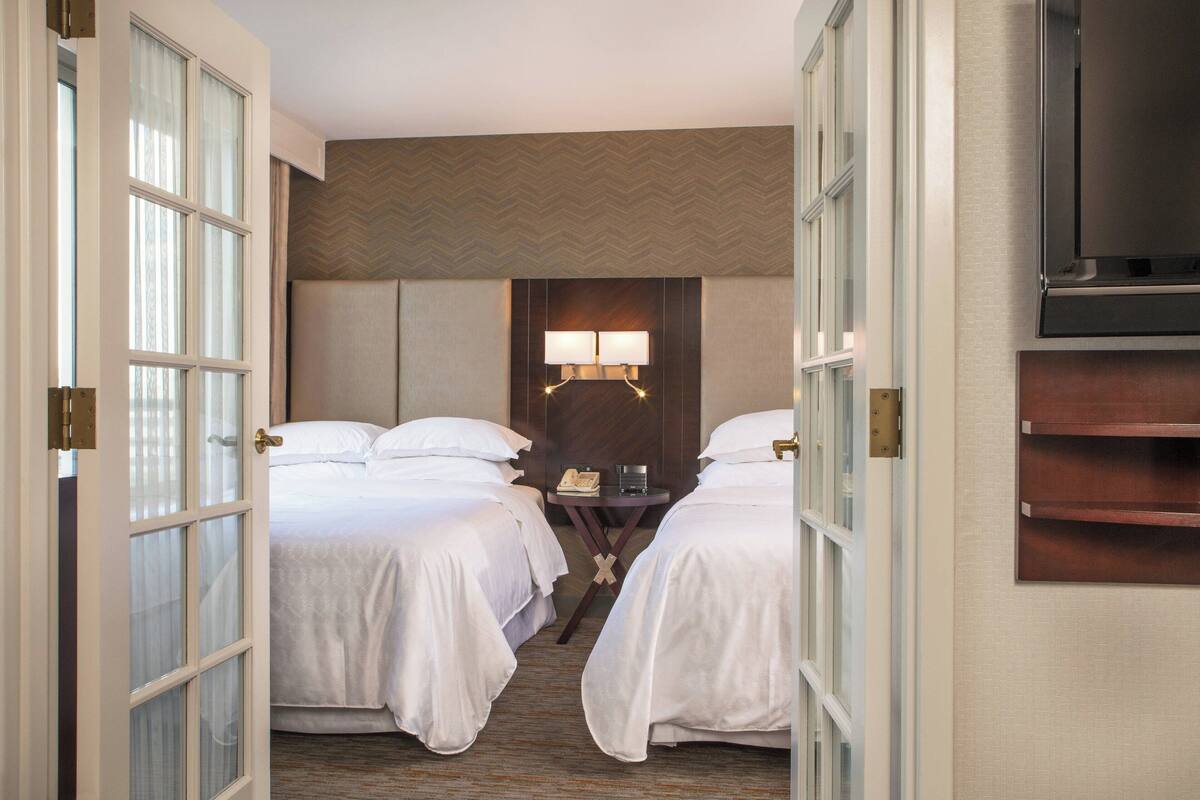 A hotel room with two beds, a nightstand with a lamp, and a television mounted on the wall.