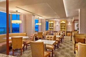 A hotel dining area with multiple tables and chairs, a view of the outdoors, and a patterned carpet. - Sheraton Suites Chicago Elk Grove (Elk Grove Village)