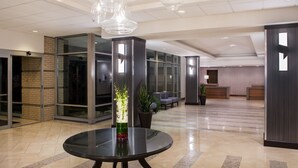Un vestíbulo moderno con una mesa redonda de vidrio, un jarrón alto con flores y un mostrador de recepción.