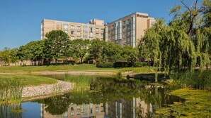 Un hotel con un edificio grande, un estanque y abundante vegetación.