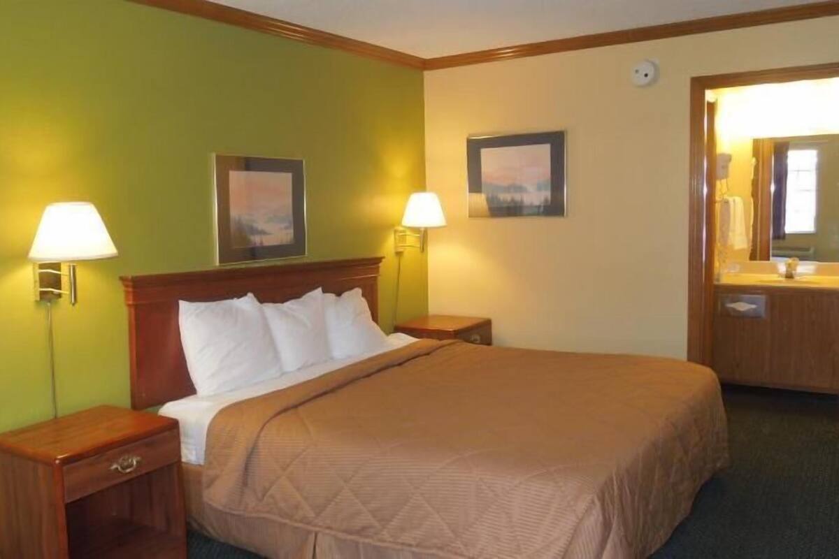 A hotel room with a bed, two bedside tables, two wall-mounted lamps, and two framed pictures.