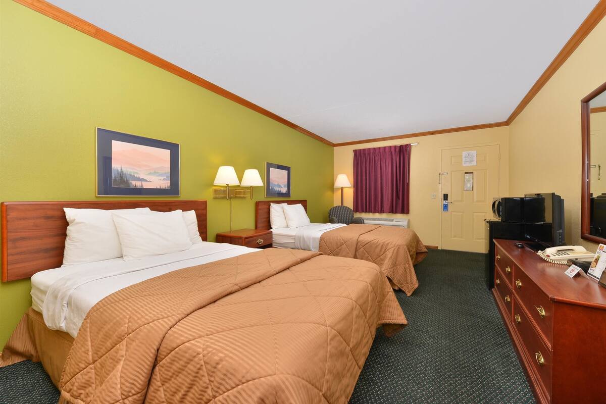 A hotel room with two beds, a desk with a telephone, a television, and two wall-mounted lamps.