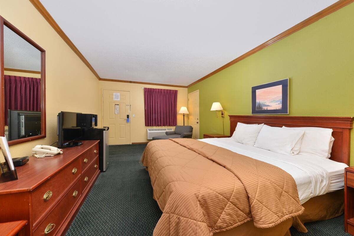 A hotel room with a bed, a desk with a telephone, a television, and a window with curtains.