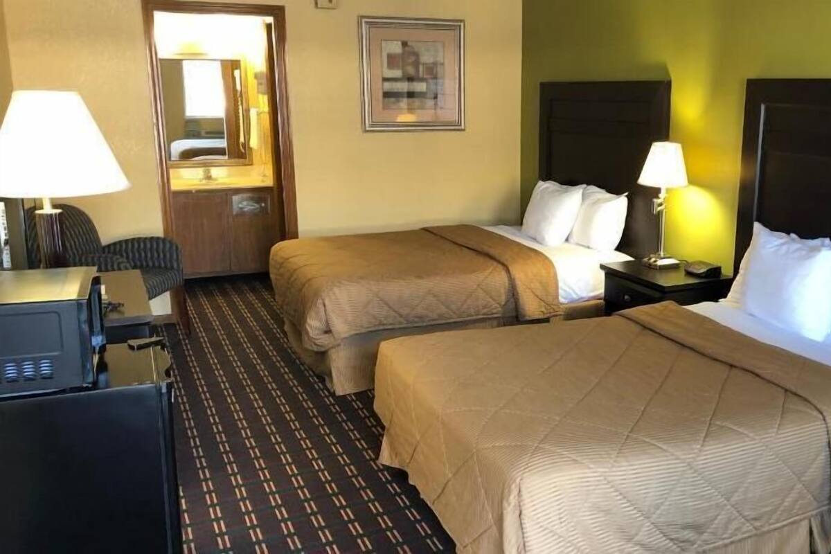 A hotel room with two beds, a desk with a lamp, a television, and a door.