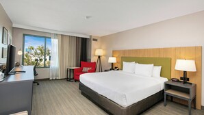 A hotel room with a large bed, a desk with a computer, a red chair, and a view of the city.