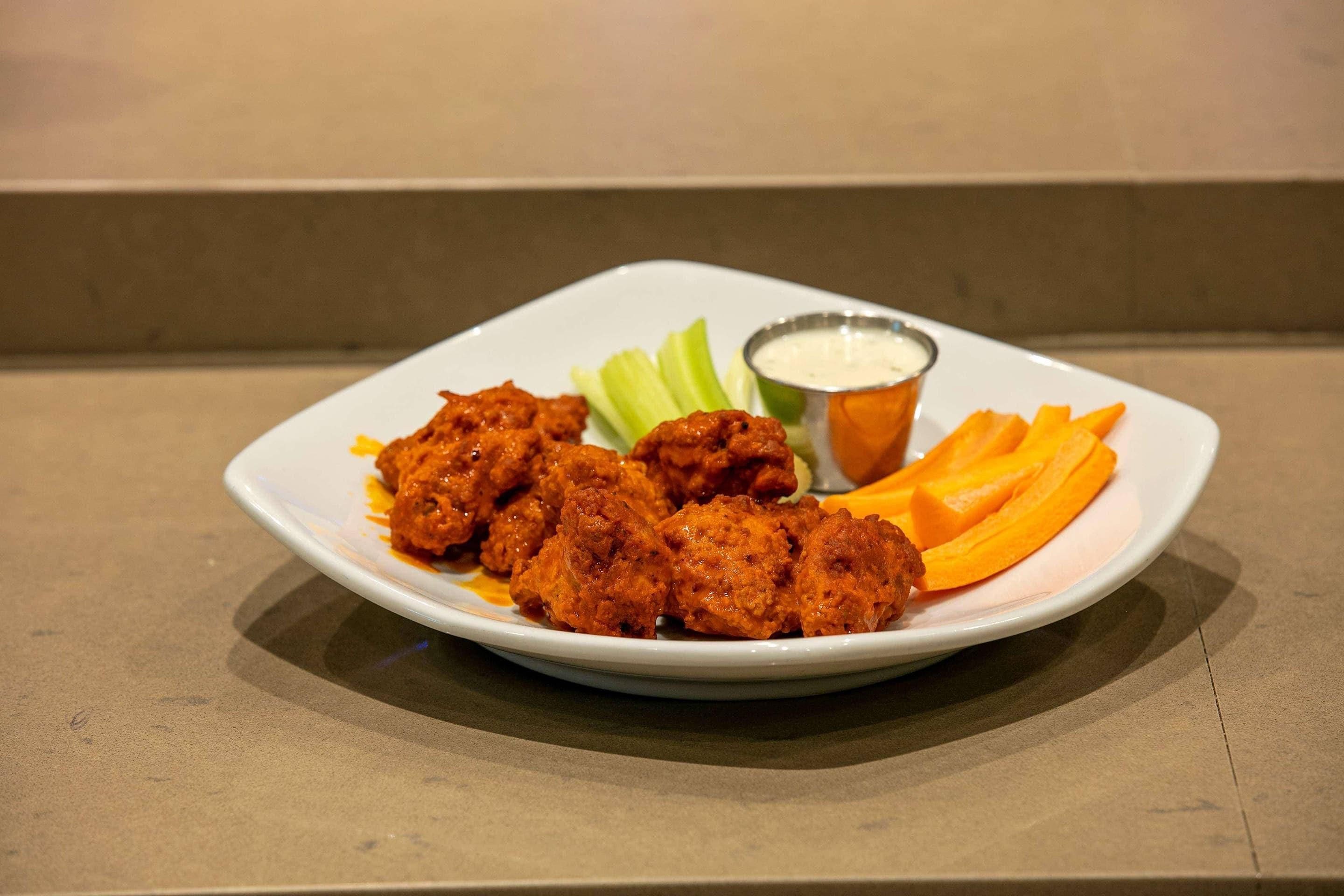 A plate of fried chicken with celery and carrots, and a small bowl of sauce.