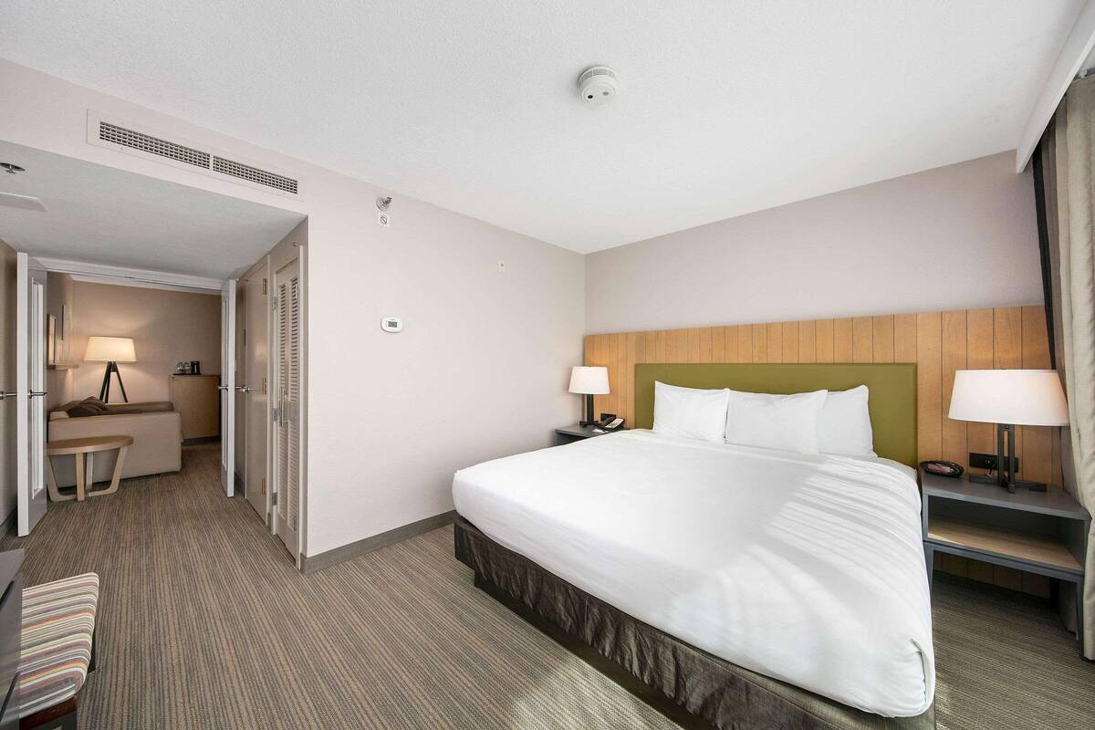Une chambre d’hôtel avec un grand lit, des tables de chevet avec des lampes, un bureau avec une chaise et une armoire.