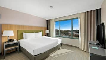 Een hotelkamer met een bed, twee nachtkastjes, een televisie en een raam met uitzicht op de stad.
